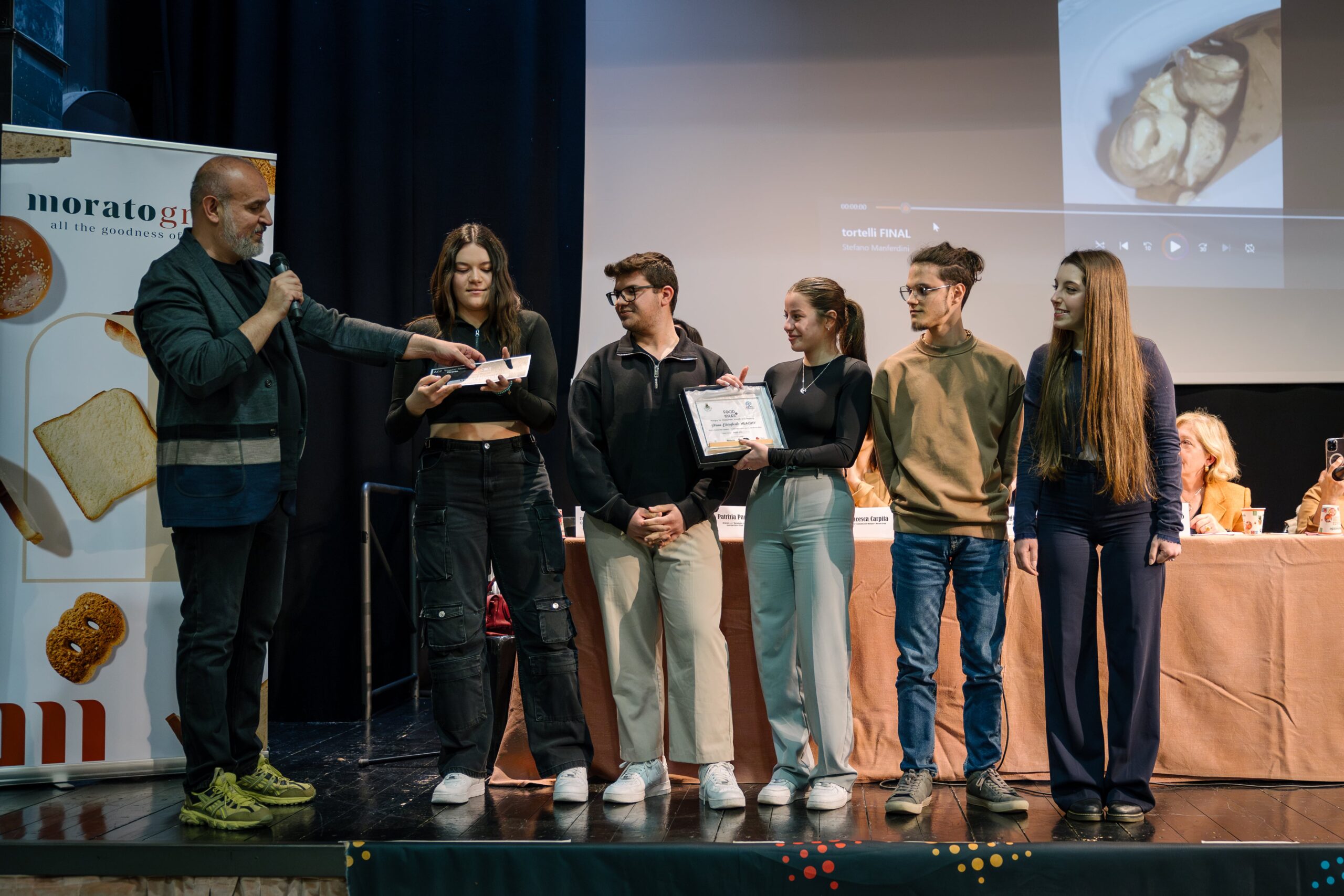 Un evento di premiazione con cinque giovani che ricevono un riconoscimento su un palco