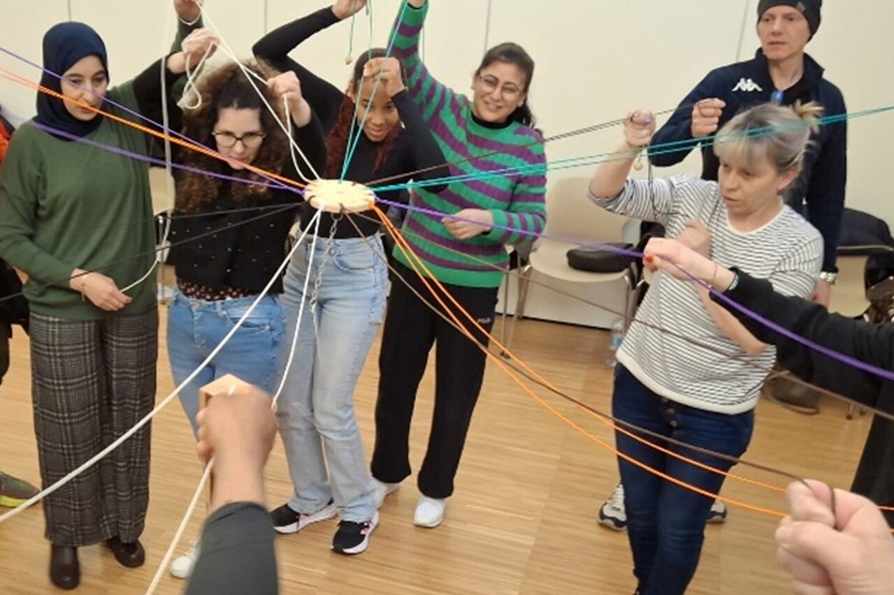 Gruppo di persone che partecipano a un'attività di team building con dei fili colorati