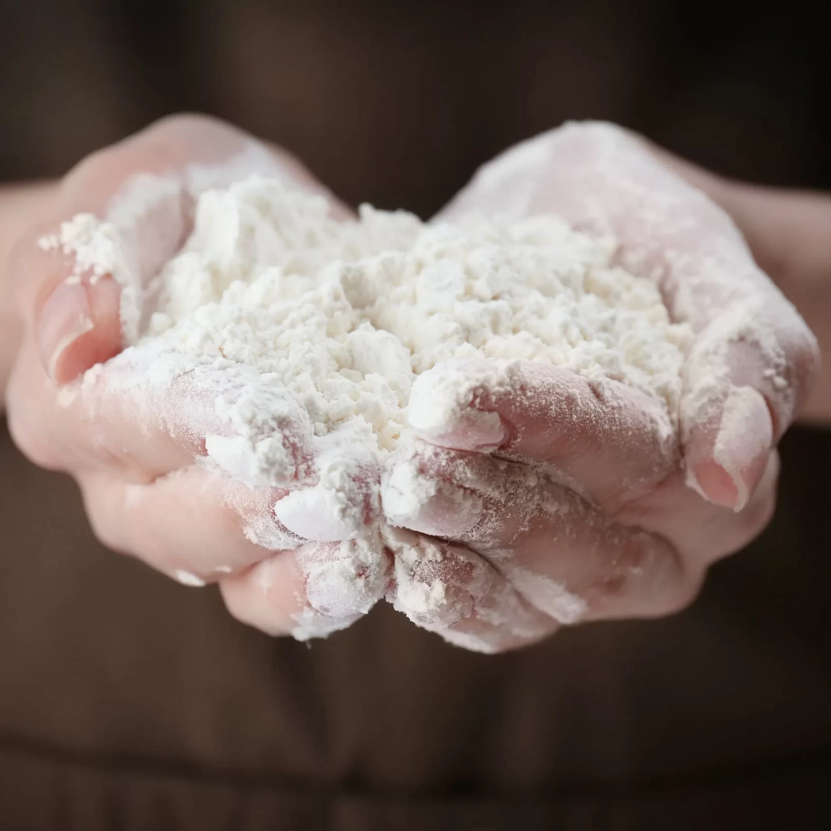Persona che tiene una manciata di farina bianca fresca per la preparazione di dolci