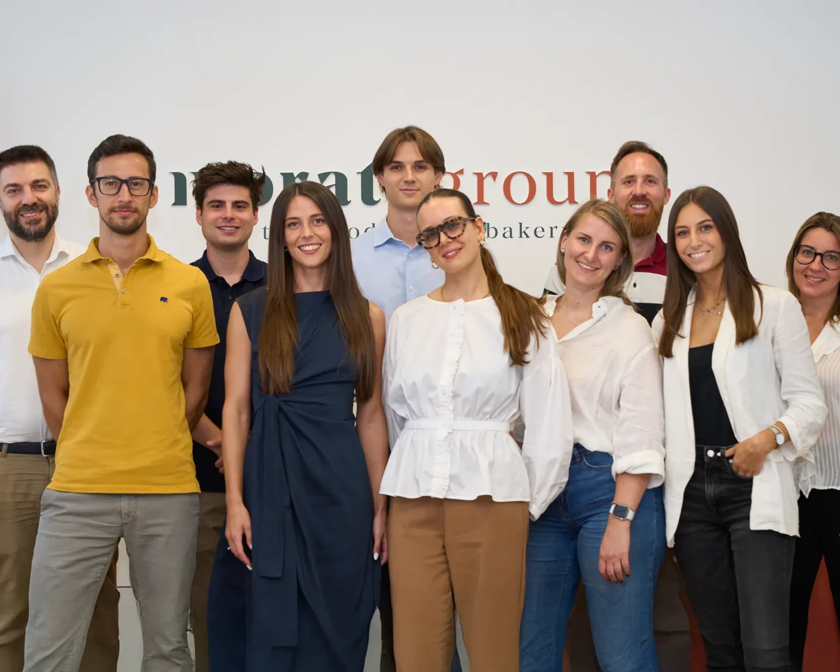 Gruppo di professionisti sorridenti in un ambiente di lavoro moderno con logo sullo sfondo