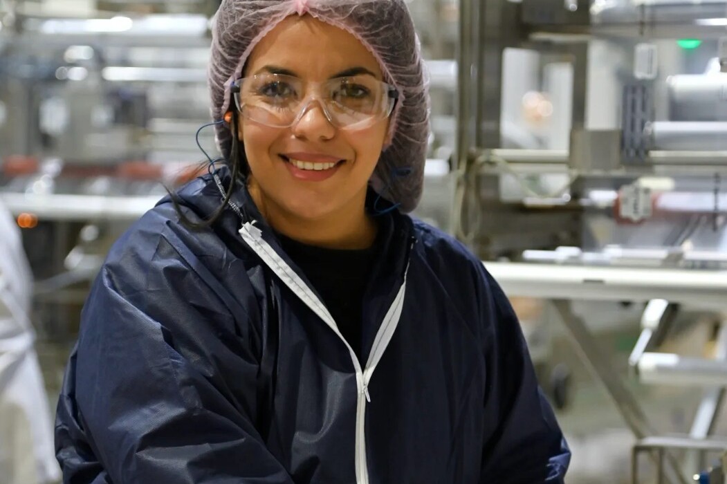 Donna sorridente con guanti e berretto in un ambiente di produzione alimentare