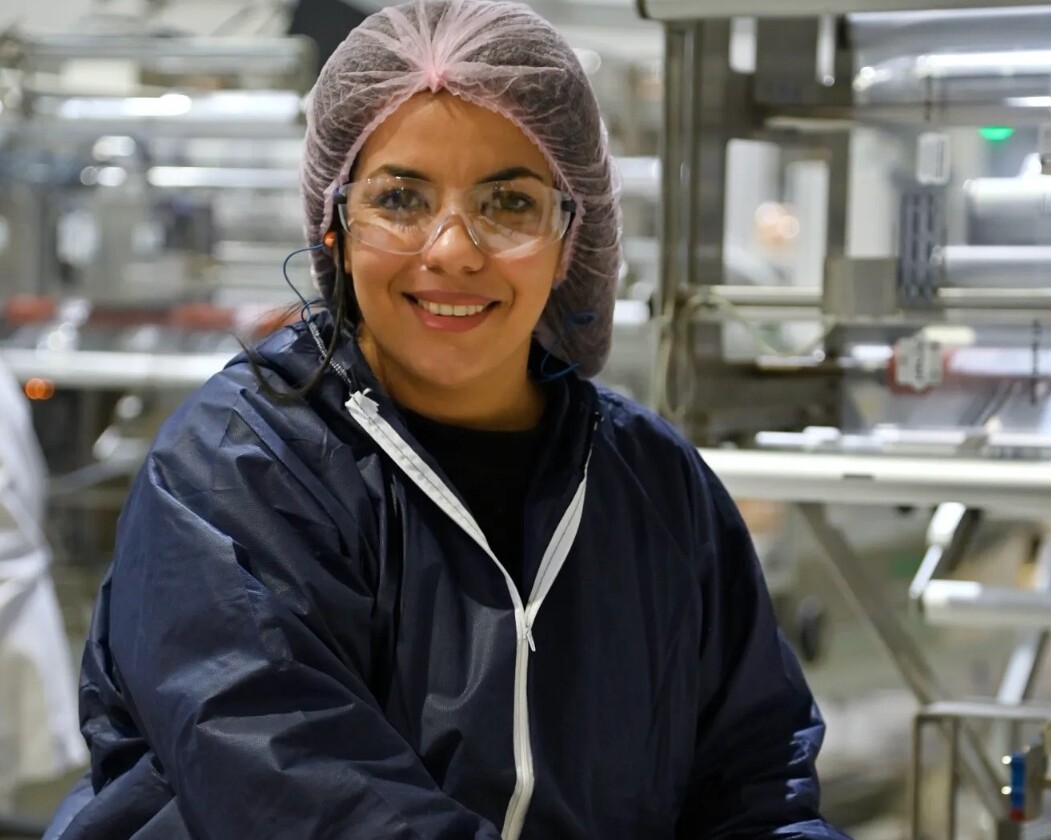 Donna sorridente con guanti e berretto in un ambiente di produzione alimentare